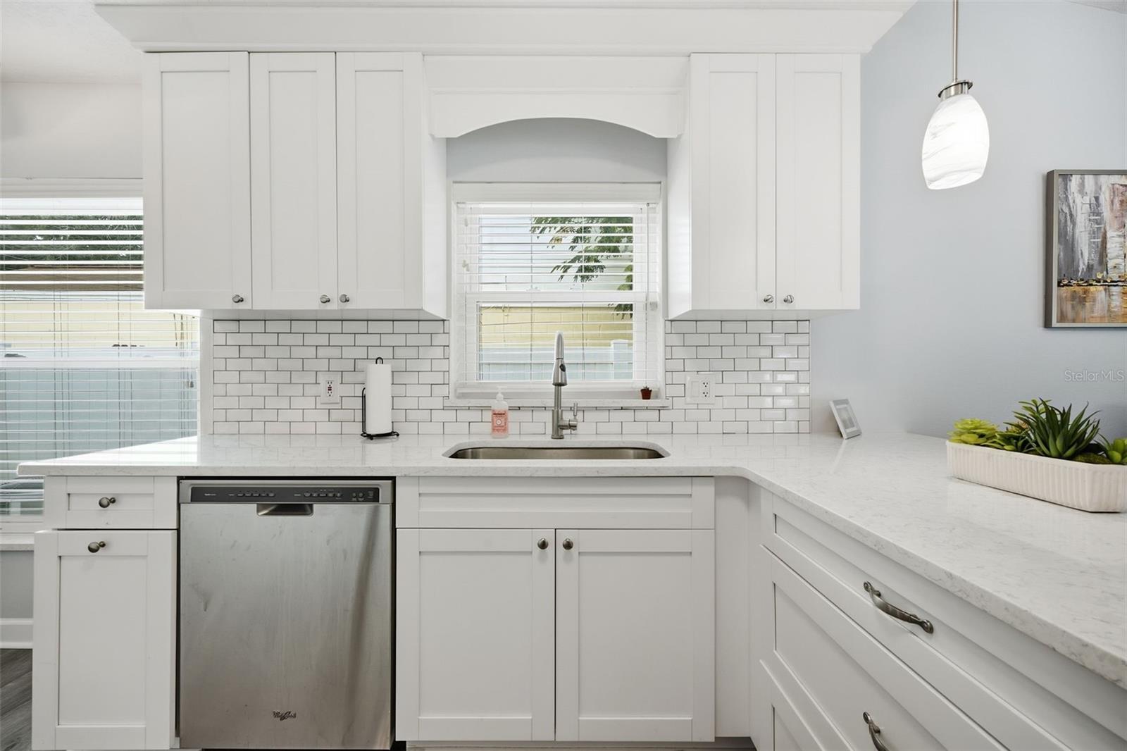 White kitchen with shaker cabinets, subway tile backsplash, stainless dishwasher, and sink beneath a window.