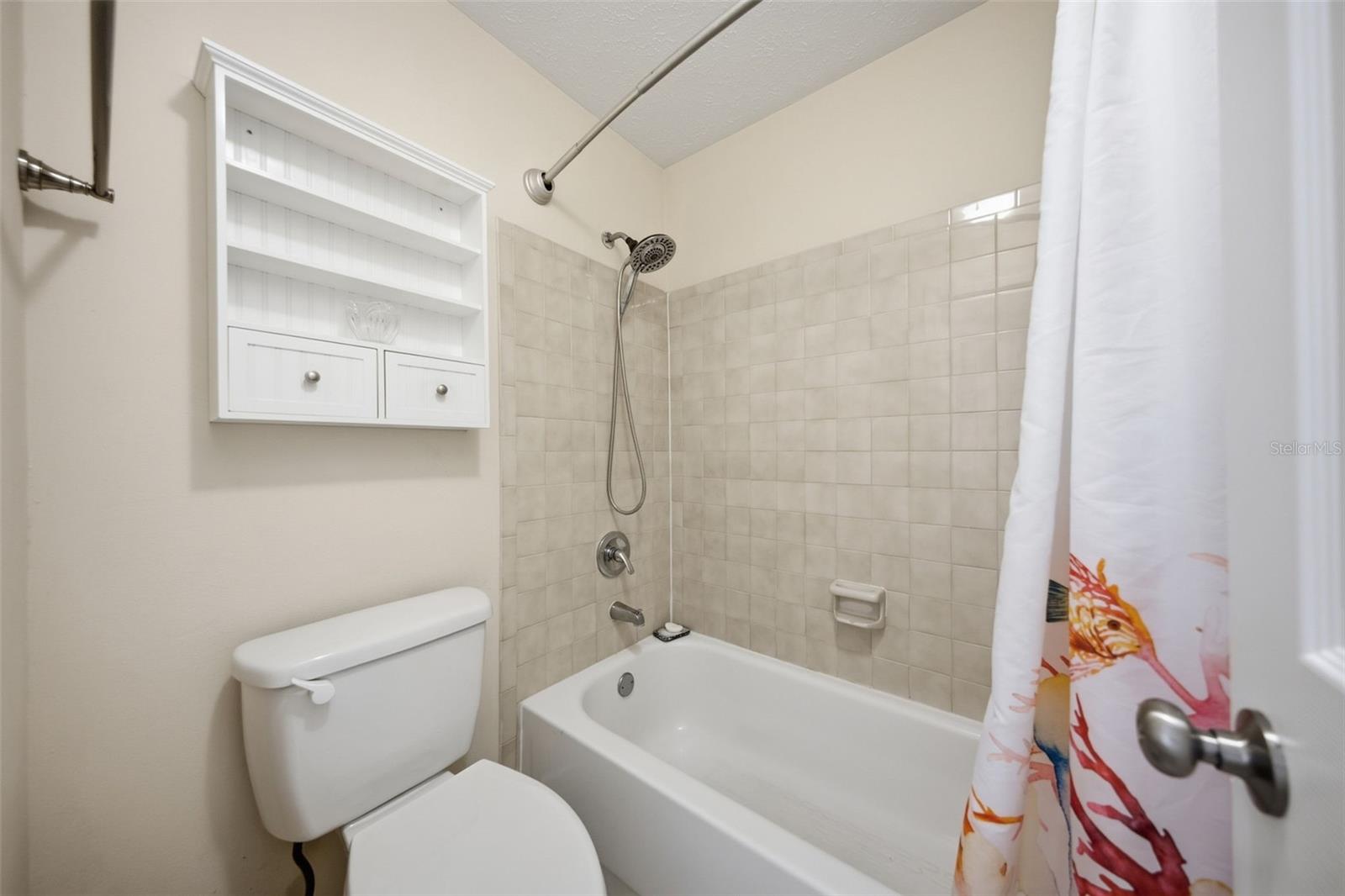 Bathroom with a tiled tub and shower, built-in shelves, and a colorful floral curtain.