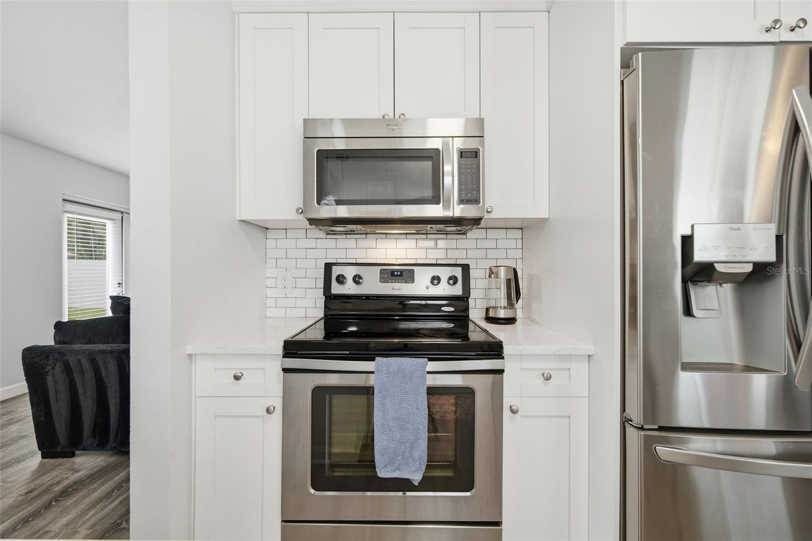 White kitchen with stainless steel appliances and subway tile backsplash, viewed toward the range and refrigerator.