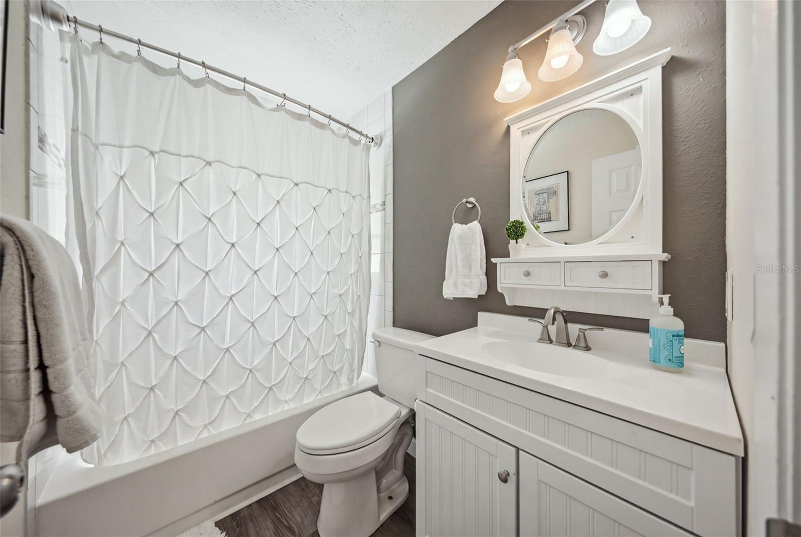 Bathroom with a white vanity, round mirror, and patterned shower curtain.
