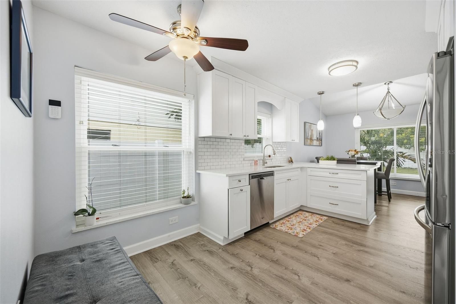 Bright white kitchen with a large island, stainless steel appliances, subway-tile backsplash, and wood-look floors.