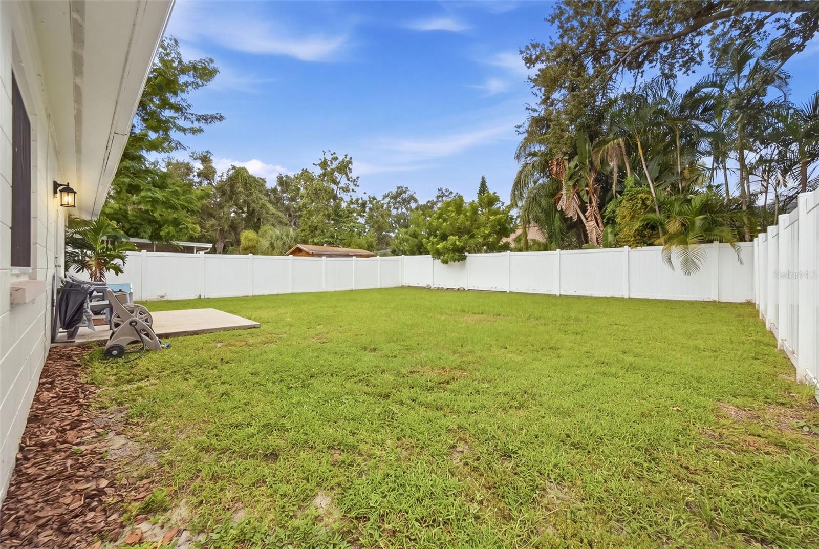 Fenced backyard with a large lawn, patio, and mature palms.