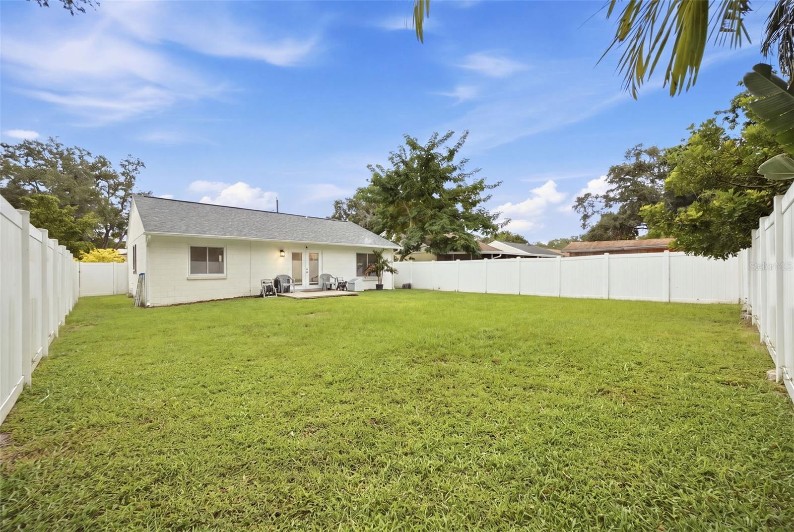 Fenced backyard with broad lawn and patio seating behind a single-story home.
