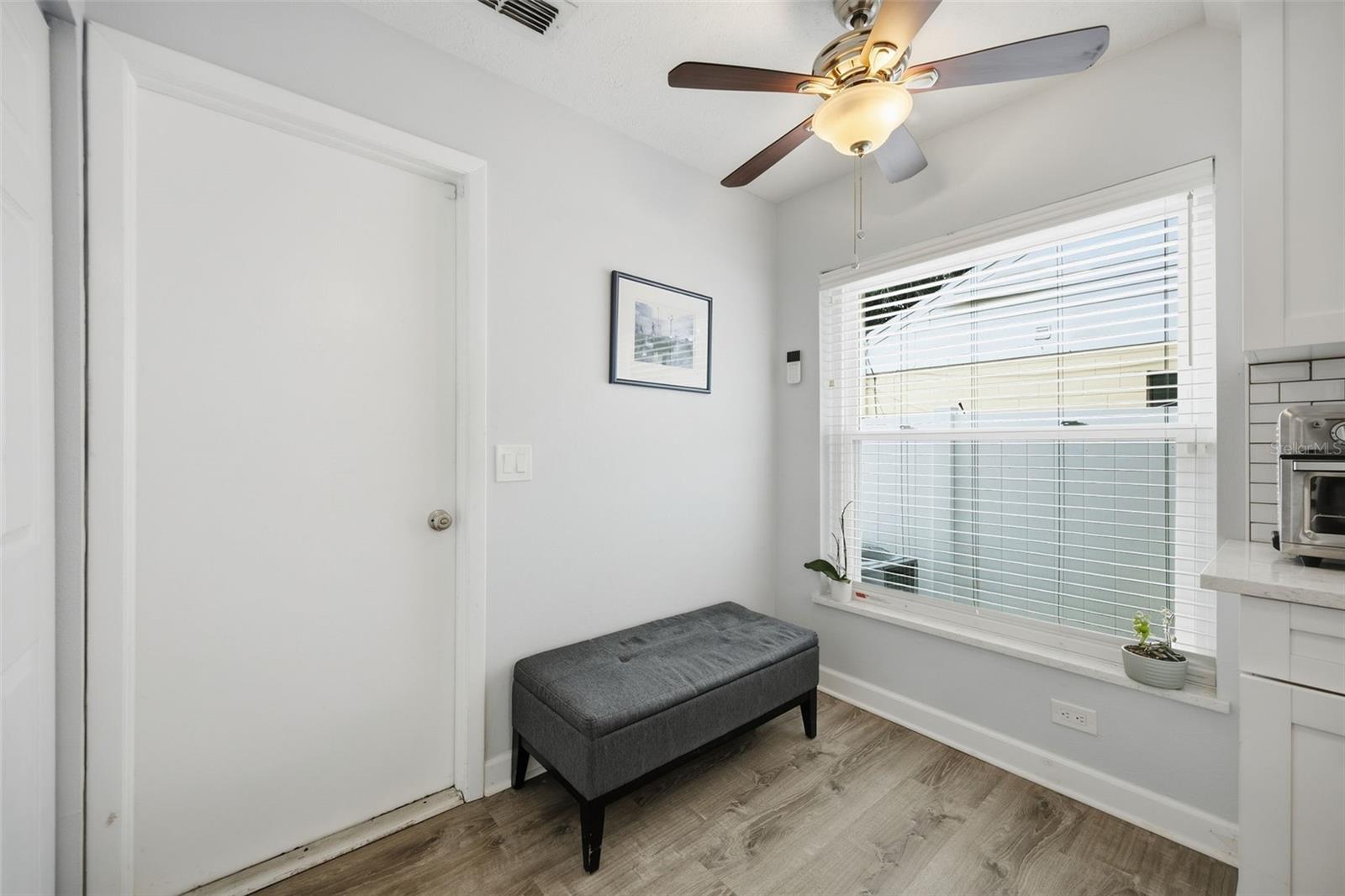 Bright kitchen nook with a gray bench beneath a wide window with white blinds.