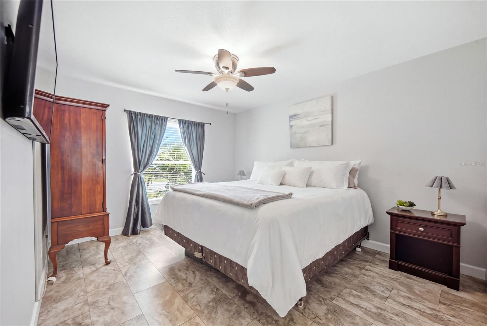Furnished bedroom with a white bed, dark wood furniture, gray curtains, and marble-look tile floor.