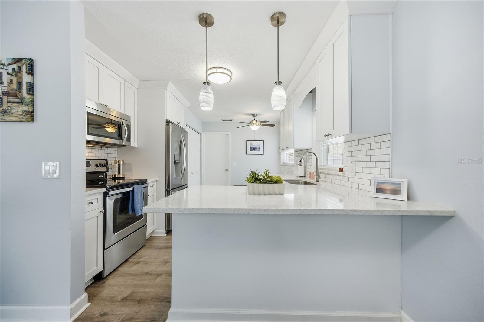 Kitchen with a large quartz island, white cabinetry, subway tile backsplash, and stainless steel appliances.
