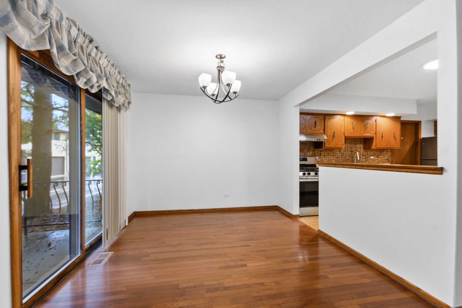 Empty dining area with hardwood floors, a chandelier, and sliding glass doors beside the kitchen.