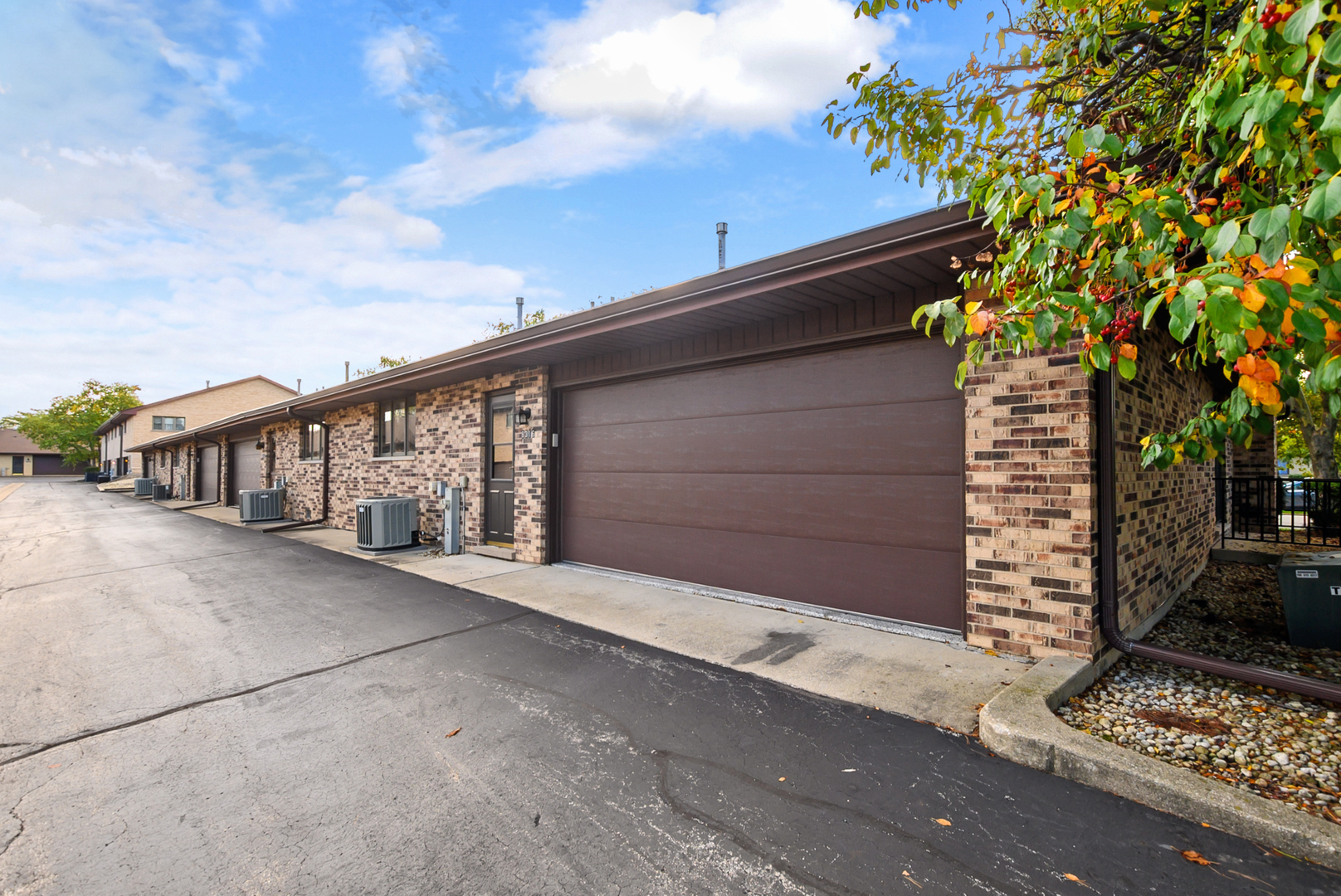 Brick townhome with a large brown garage door and autumn foliage.