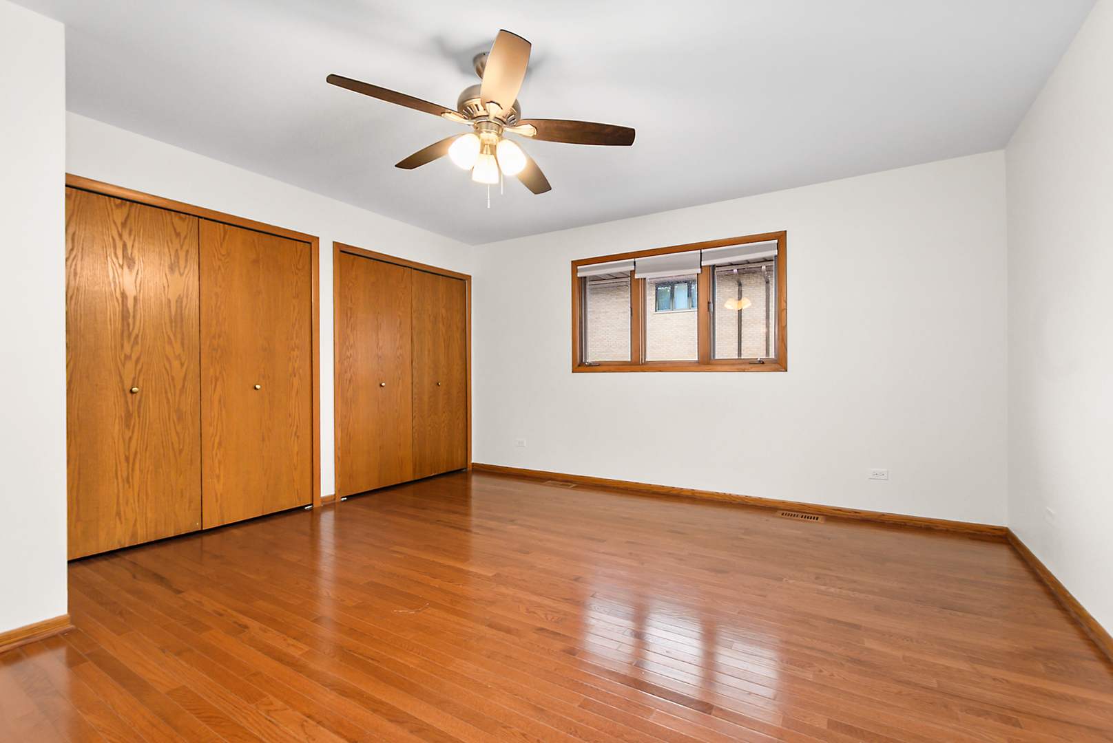 Vacant bedroom with hardwood floors, two wooden closets, and a ceiling fan.
