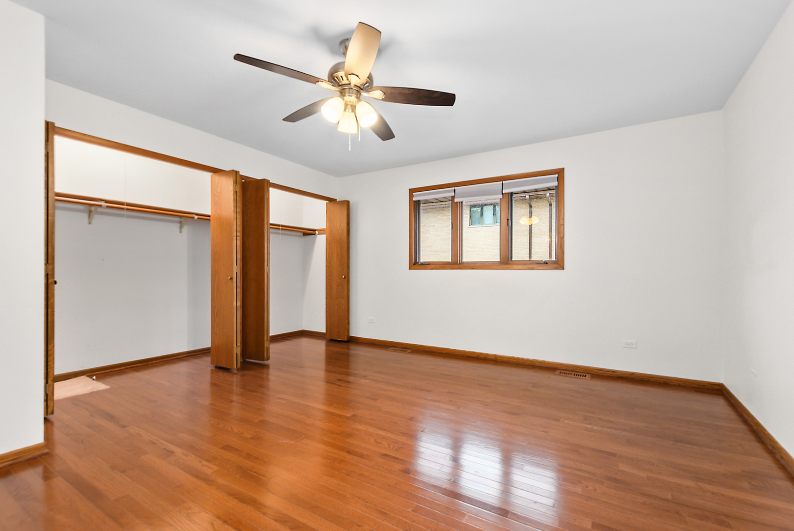 Empty bedroom with hardwood floors, open wooden closets, and a ceiling fan.