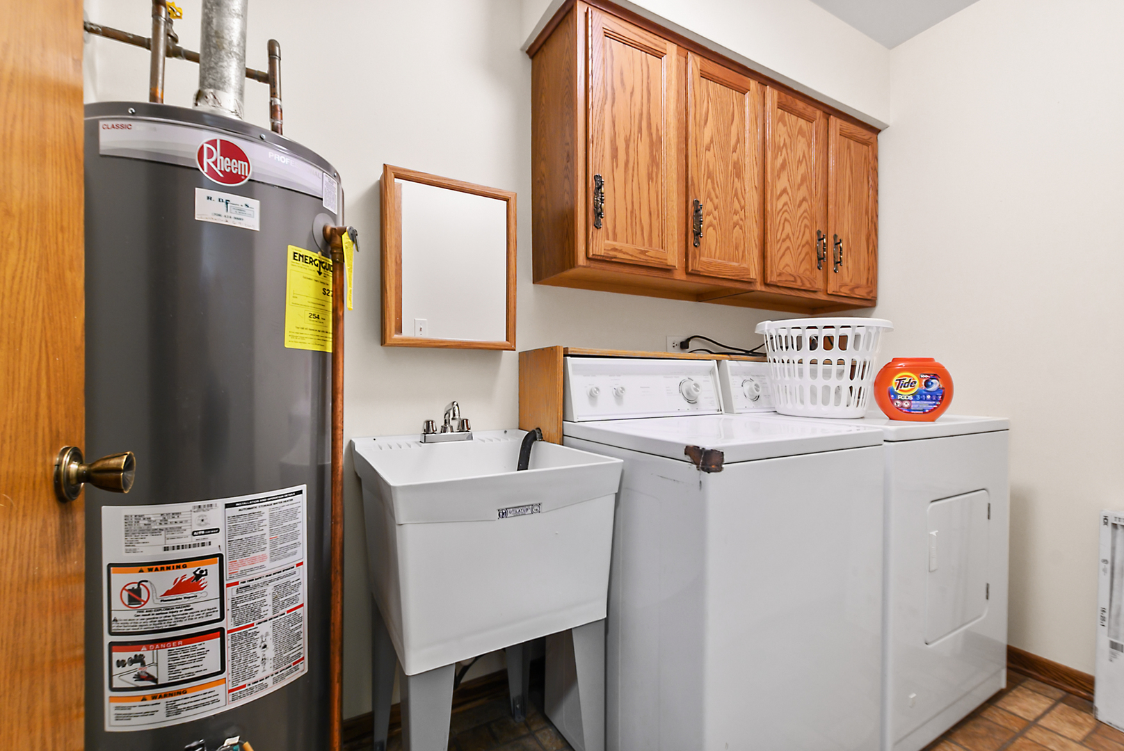 Laundry room with washer, dryer, utility sink, Rheem water heater, and oak cabinets.