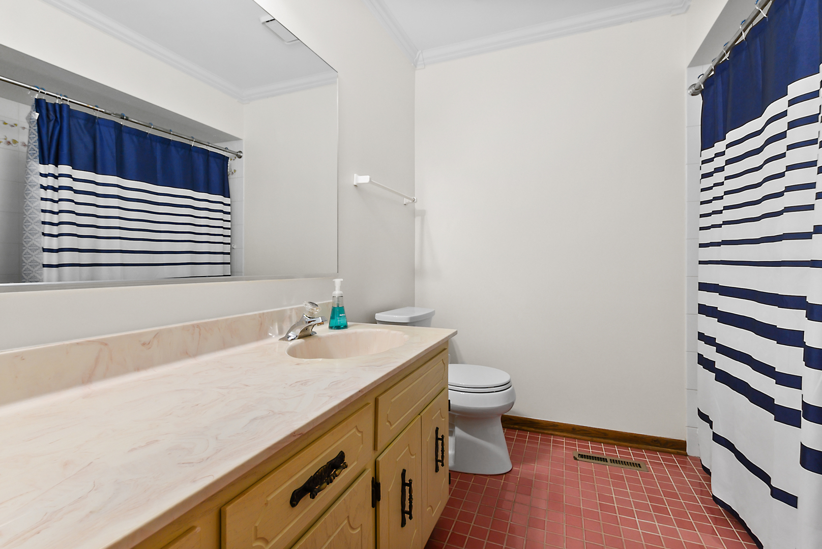Bathroom with a long vanity, wood cabinets, red tile floor, and blue-and-white striped shower curtains.