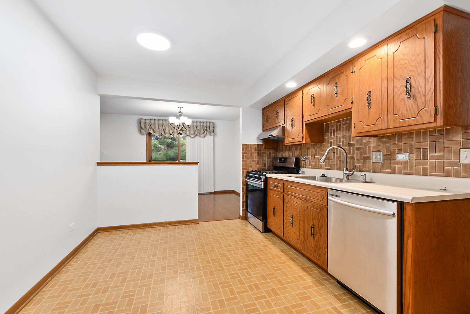 Kitchen with wood cabinets, brown tile backsplash, and stainless steel appliances.