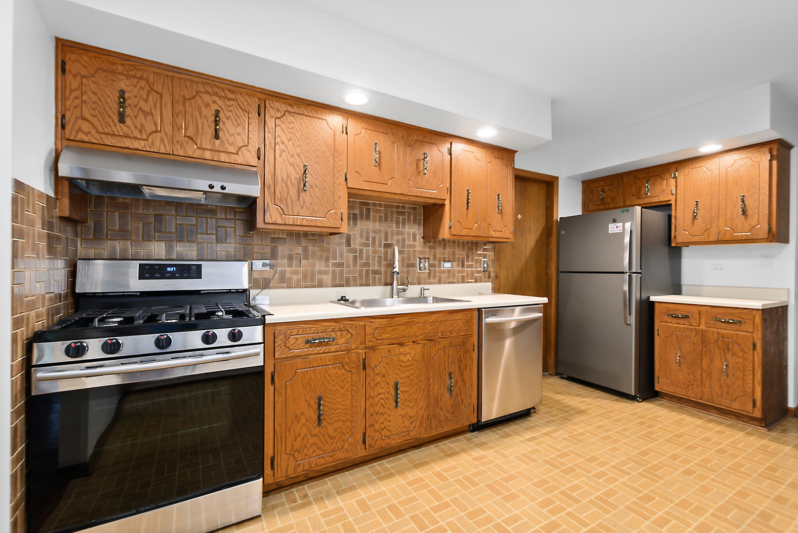 Kitchen with wood cabinets, stainless steel appliances, and brown tile backsplash.