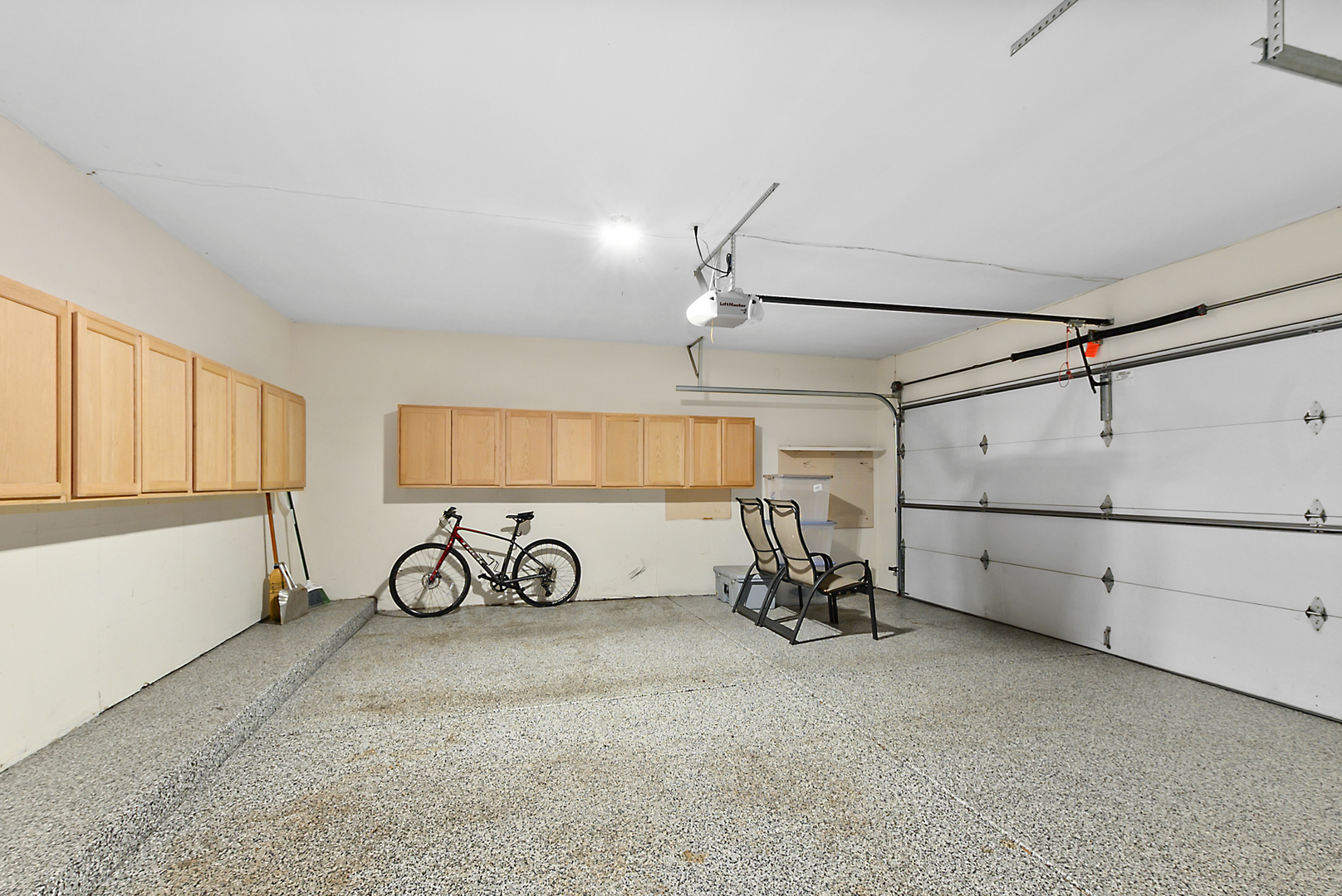 Garage with wooden storage cabinets, a speckled floor, and a bicycle beside the overhead door.