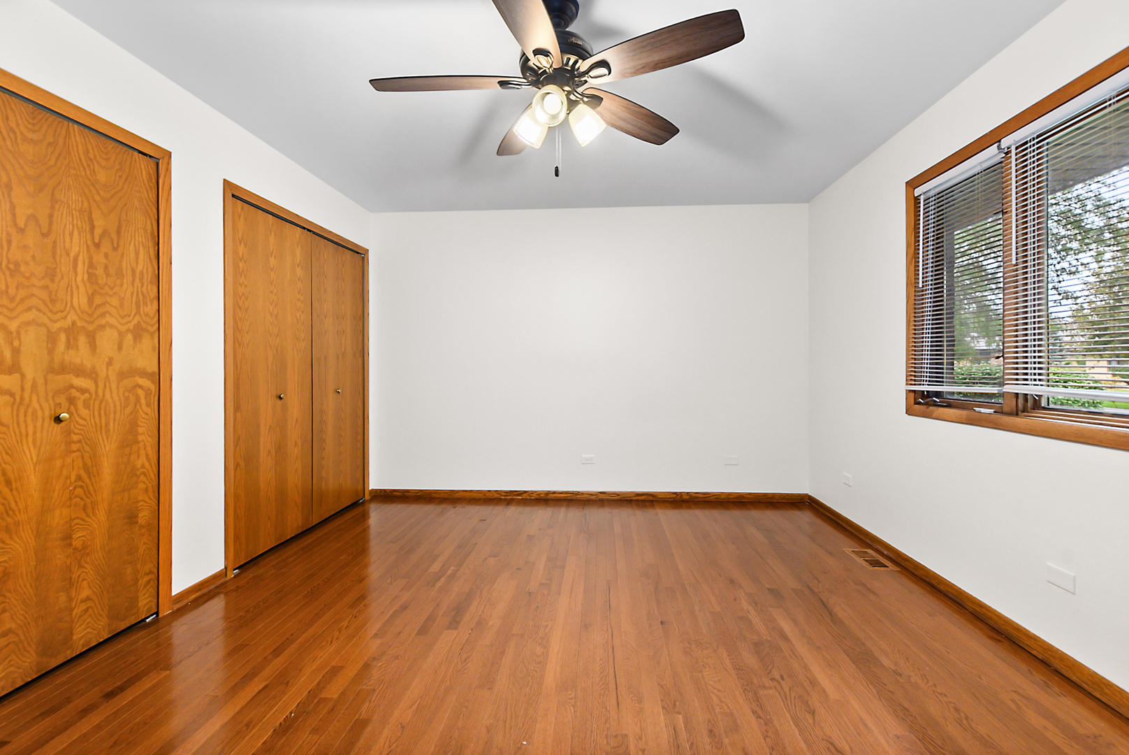 Empty bedroom with hardwood floors, wooden closet doors, and a ceiling fan.