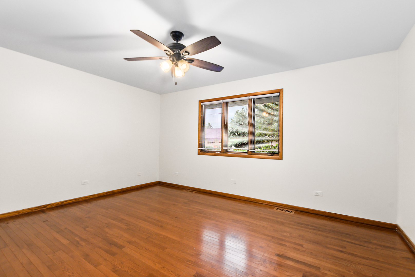 Empty room with hardwood floors, a wood-trimmed window, and a ceiling fan with lights.