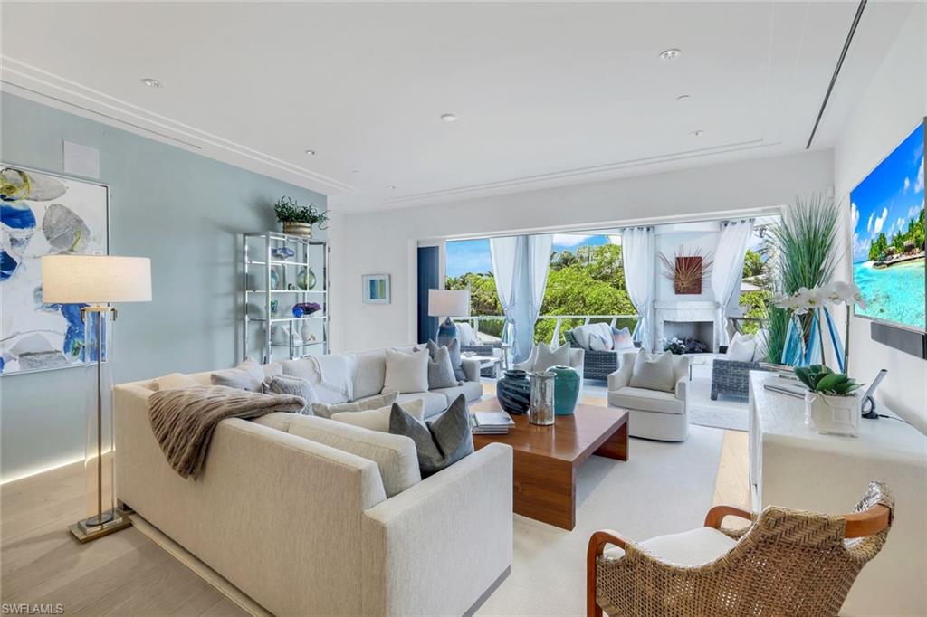 Bright living room with white sofas, a wood coffee table, and windows overlooking lush greenery.