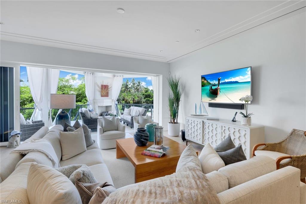 Furnished living room with white sofas and sliding doors opening to a tree-lined balcony.