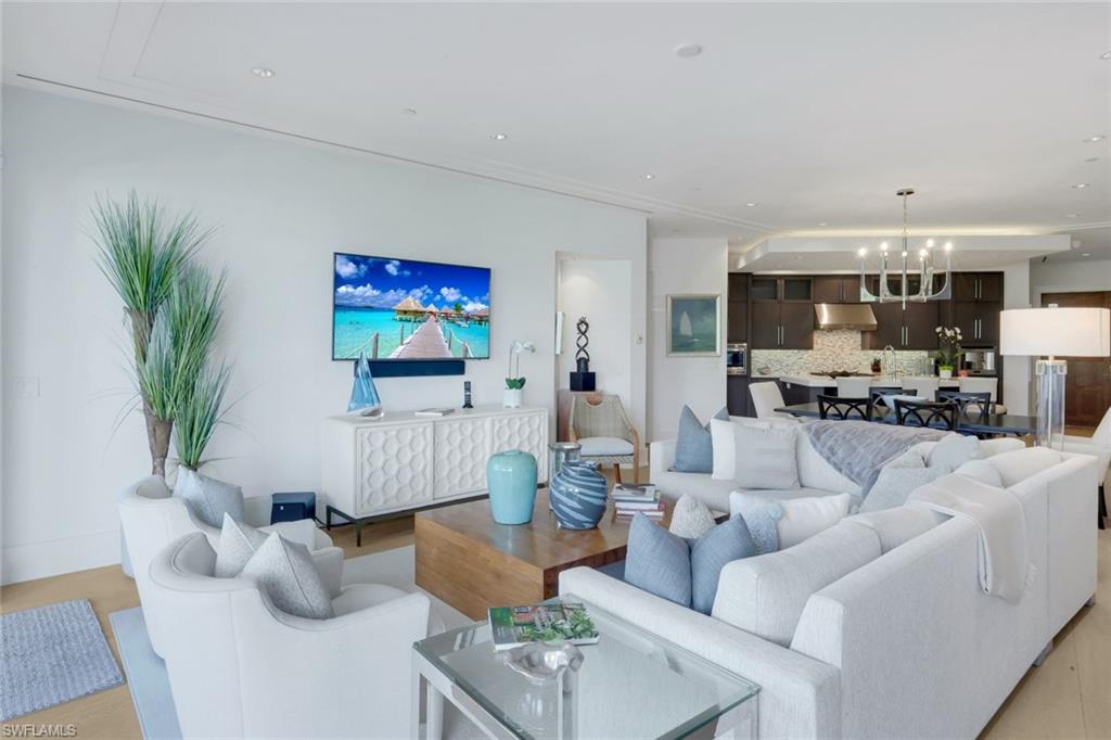 Furnished living room with white seating, coastal accents, and an open kitchen beyond.