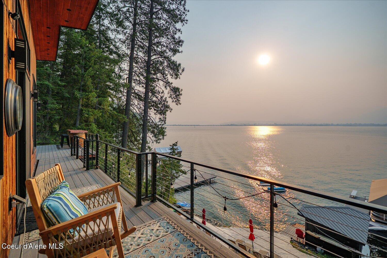 Lakeside deck with wooden chairs and patterned rugs overlooking sunlit water.