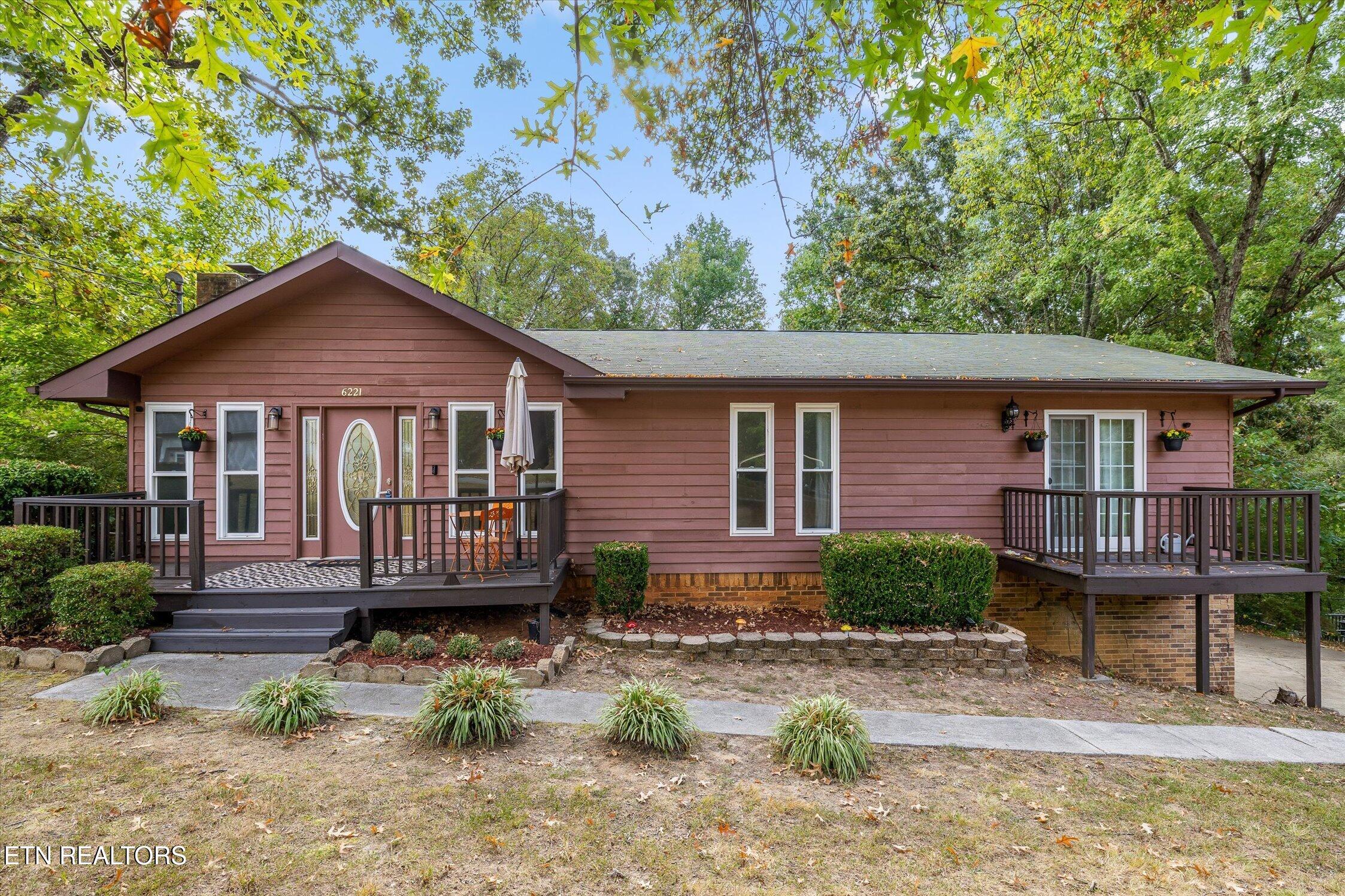Single-story mauve house with two raised decks beneath a canopy of mature trees.