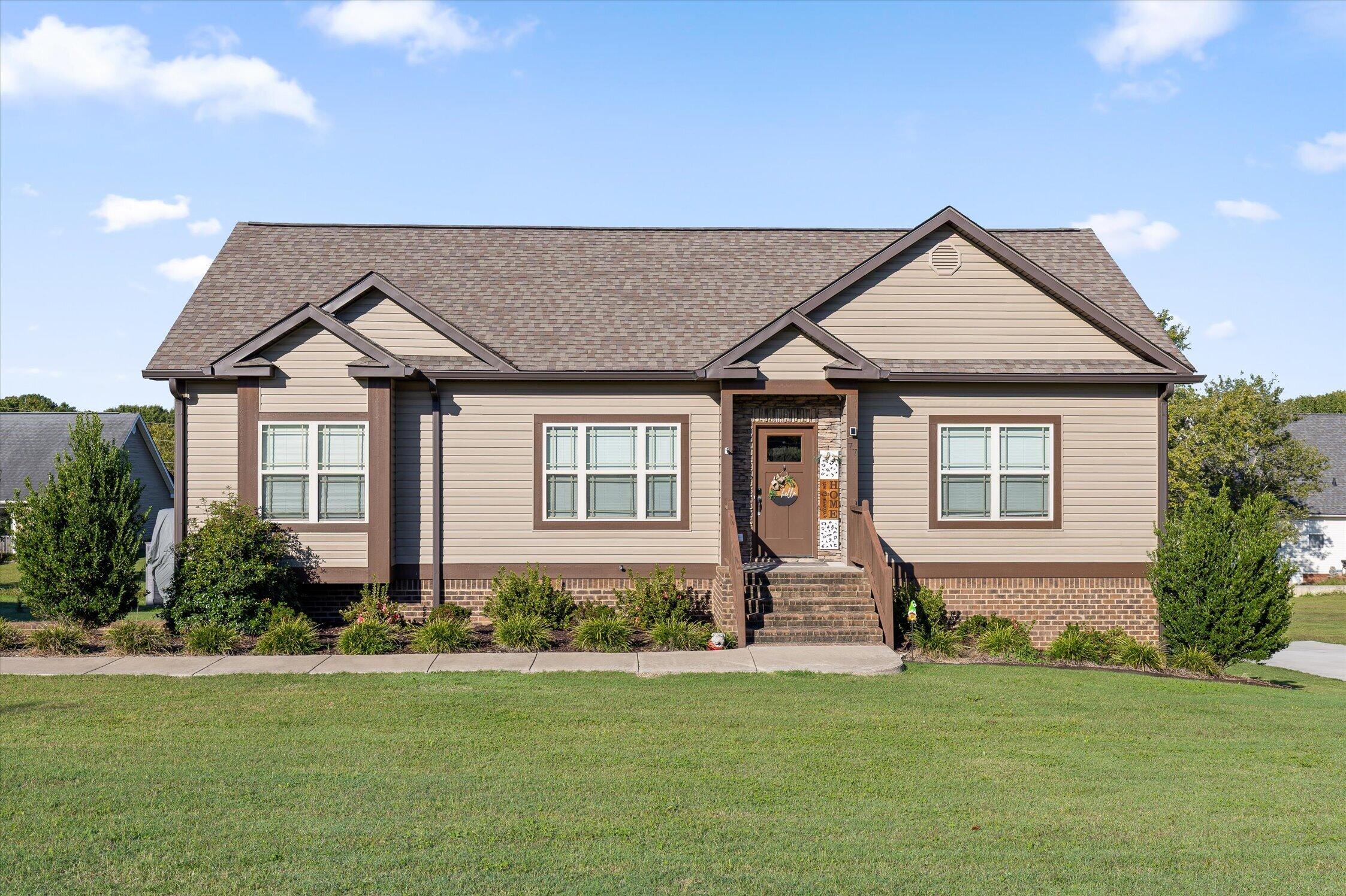 Beige single-story home with multiple gables, brick steps, and a broad front lawn.