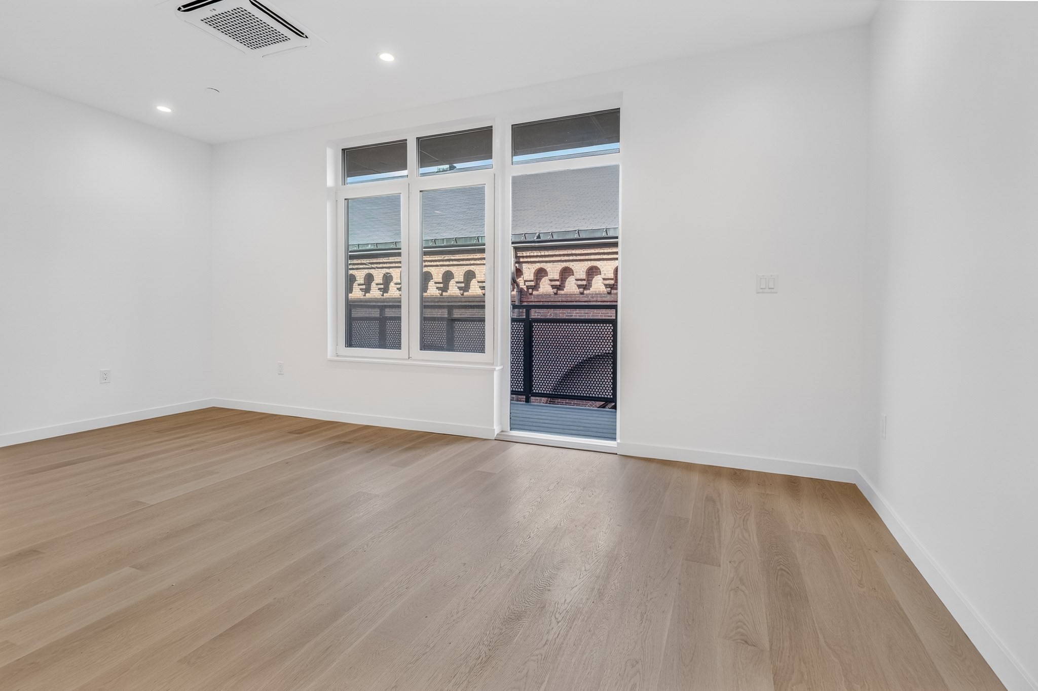 Vacant room with light wood floors, large windows, and a balcony door.