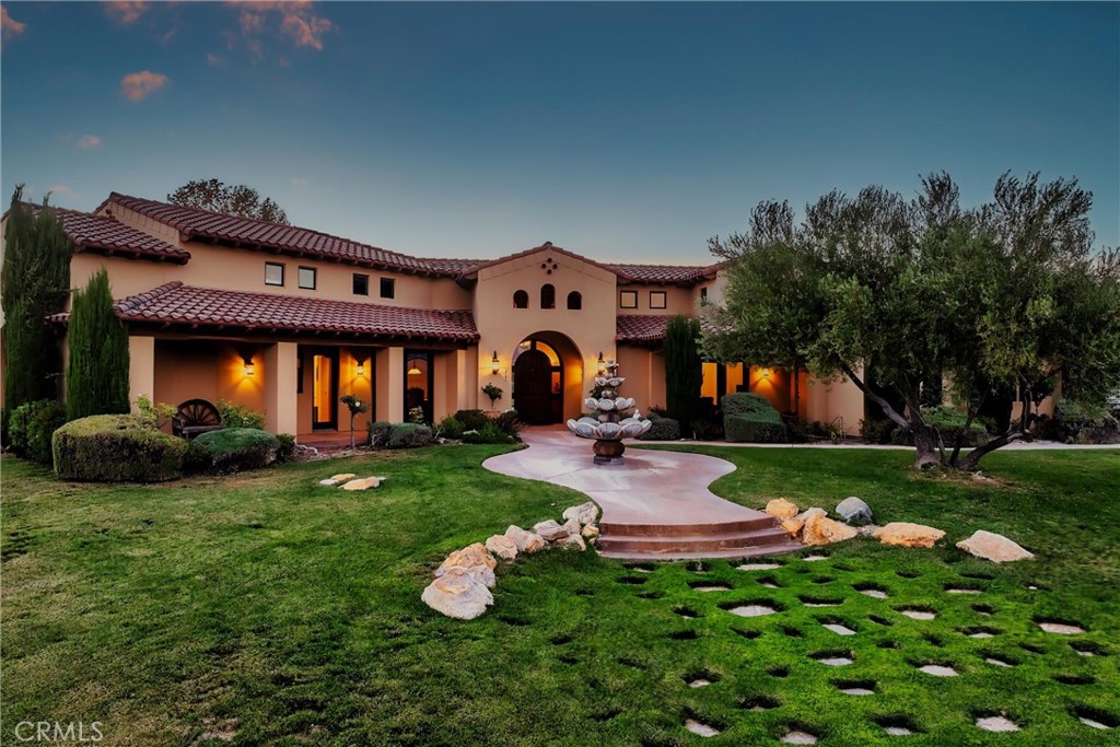 Spanish-style home with tiled roofs, an arched entry, a fountain, and landscaped lawn.