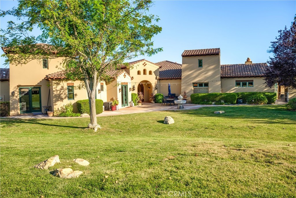 Tan stucco home with terracotta tile roofs, an arched entry, patio seating, and a broad lawn.