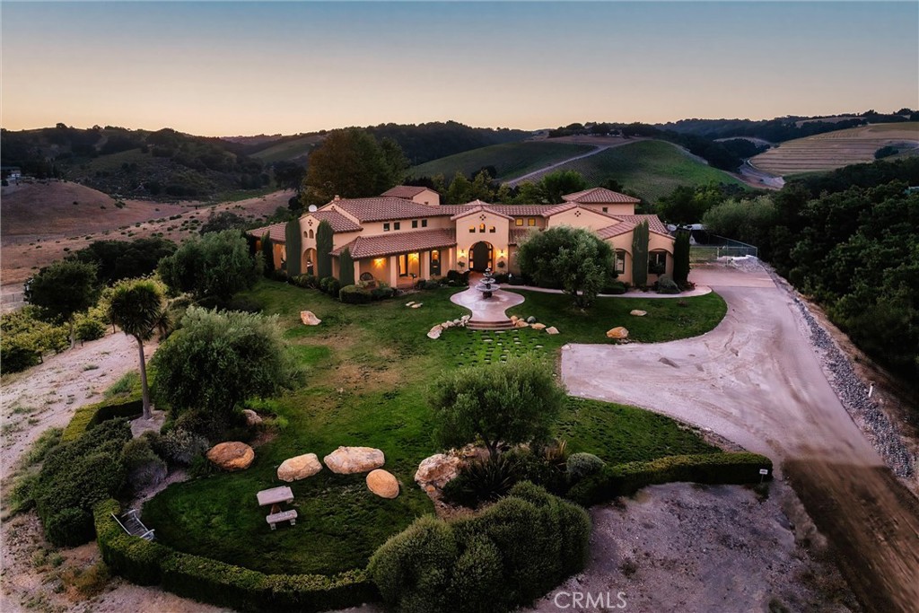 Aerial view of a Spanish-style home with landscaped grounds and rolling hills at dusk.