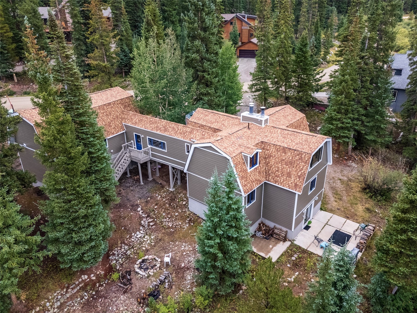 Aerial view of a gray multi-story home with a tan shingle roof among tall evergreen trees.