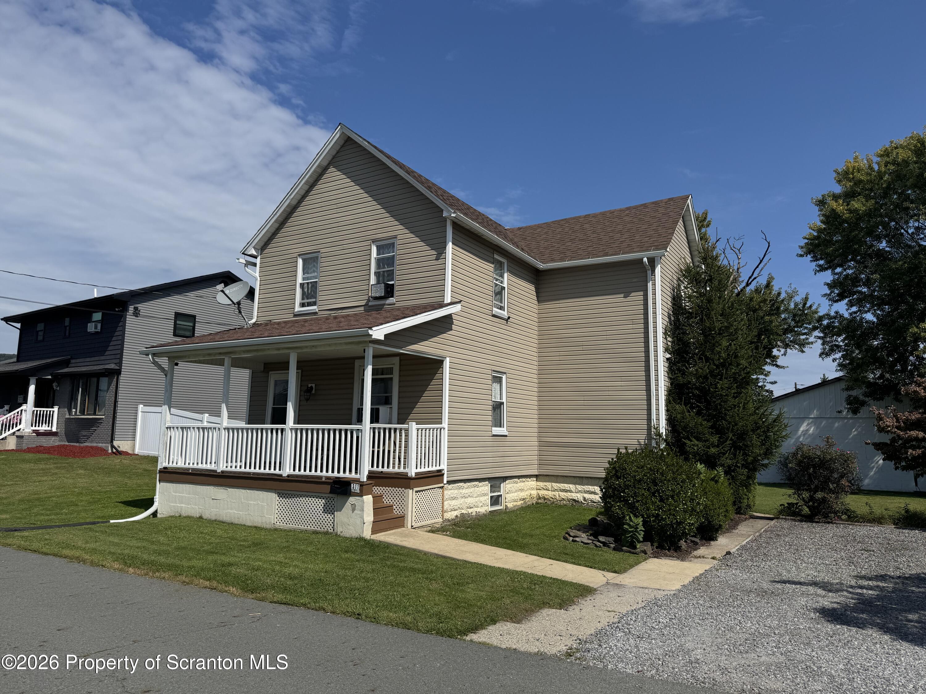 Two-story beige-sided home with a covered white-railed porch and front lawn.