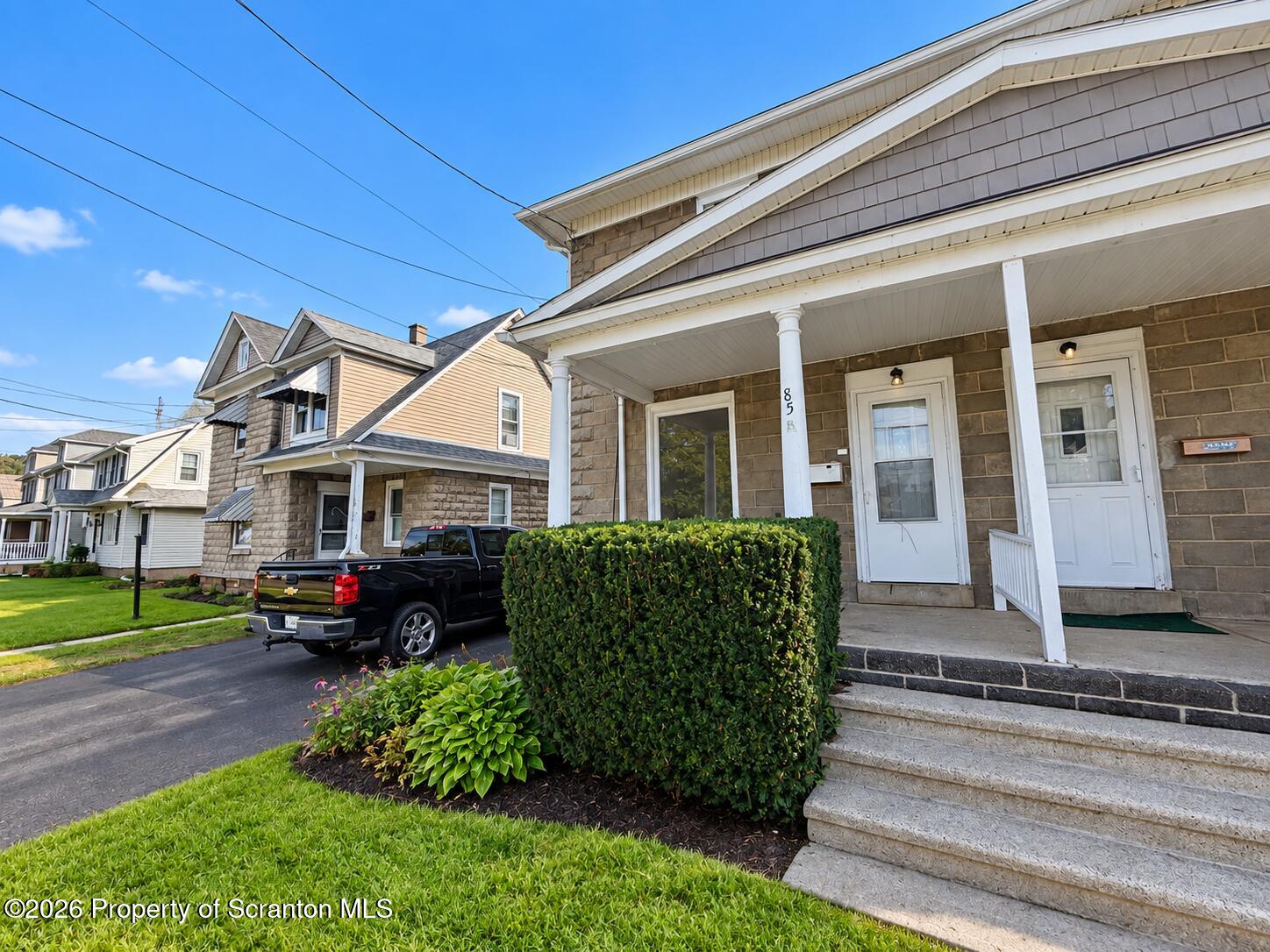 Stone-faced home with a covered porch, white columns, front steps, and trimmed hedges.