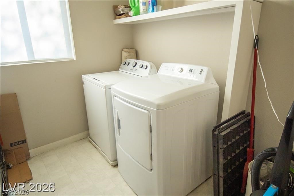 Laundry room with a white washer and dryer beneath a wall shelf.