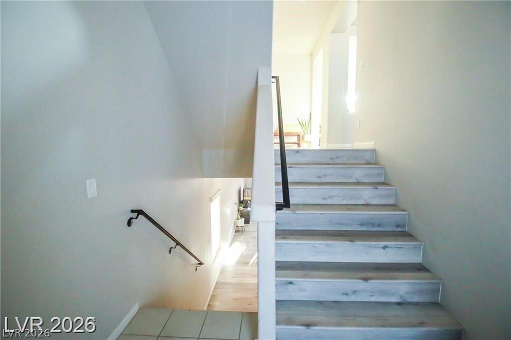 Staircase with pale wood-look treads and a black handrail leading to a bright landing.