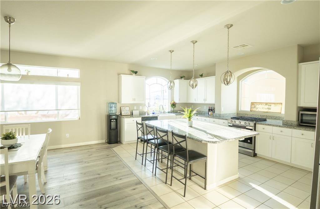 Bright kitchen with a granite island, bar stools, white cabinets, and adjoining dining area.