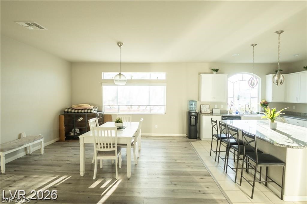 Open-plan dining area and kitchen with a white table, breakfast bar, and wood-look floors.