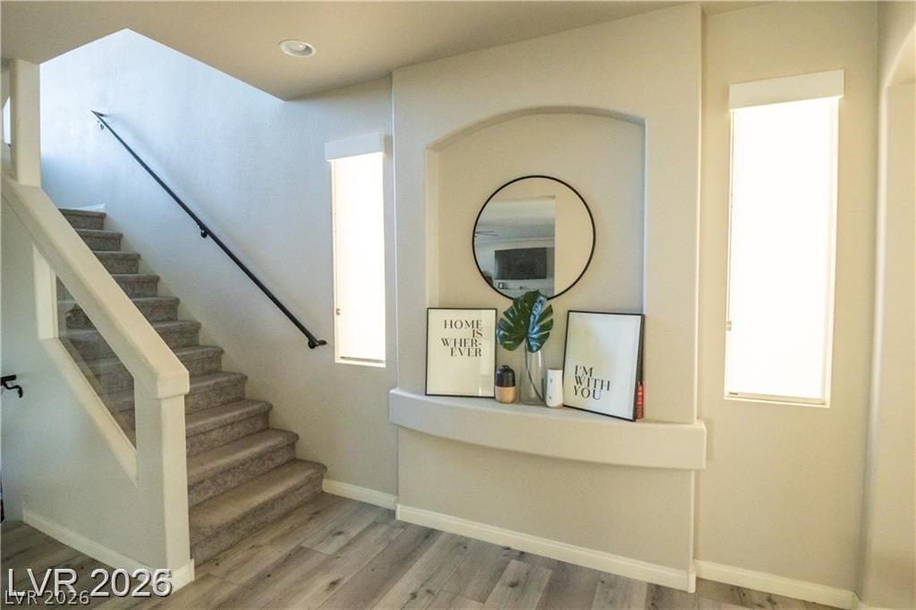 Entryway with carpeted staircase, black handrail, and recessed shelf with a round mirror.