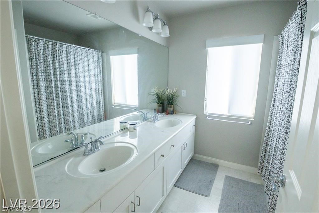 Bathroom with a long double-sink vanity, large mirror, and patterned shower curtains.