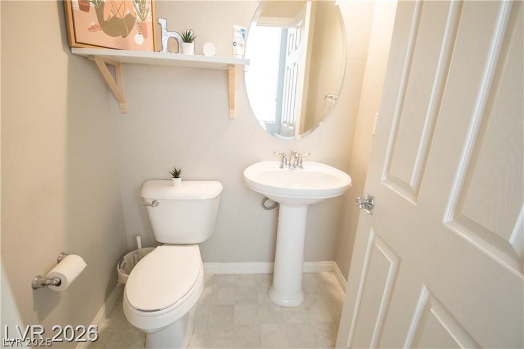 Bathroom with a pedestal sink, oval mirror, and toilet beneath a wall shelf.