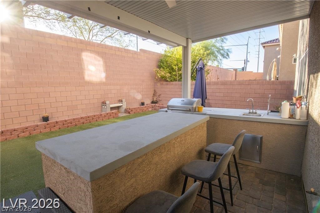 Covered patio with an outdoor kitchen, bar seating, built-in grill, and sink.