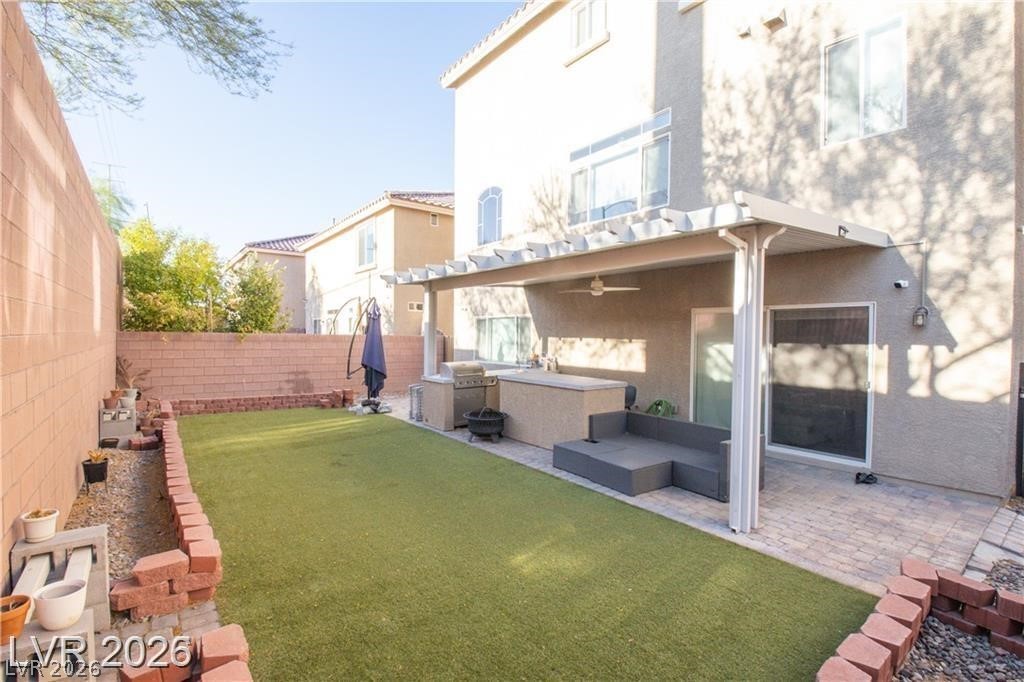 Backyard with artificial turf, covered patio, outdoor kitchen, and built-in seating.