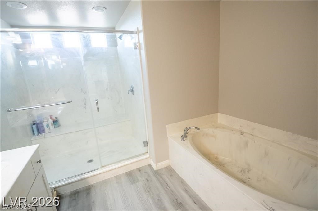 Bathroom with a glass-enclosed shower, marble-look soaking tub, and gray wood-look flooring.