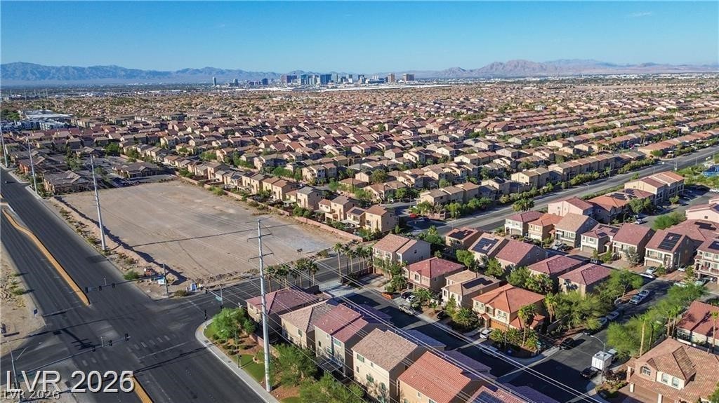 Aerial view of a Las Vegas neighborhood, with a vacant corner lot, distant skyline, and mountains.