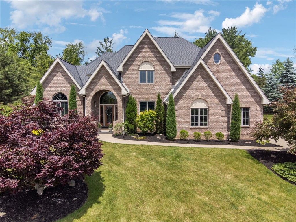 Brick home with multiple gables, an arched entry, landscaped gardens, and a broad lawn.
