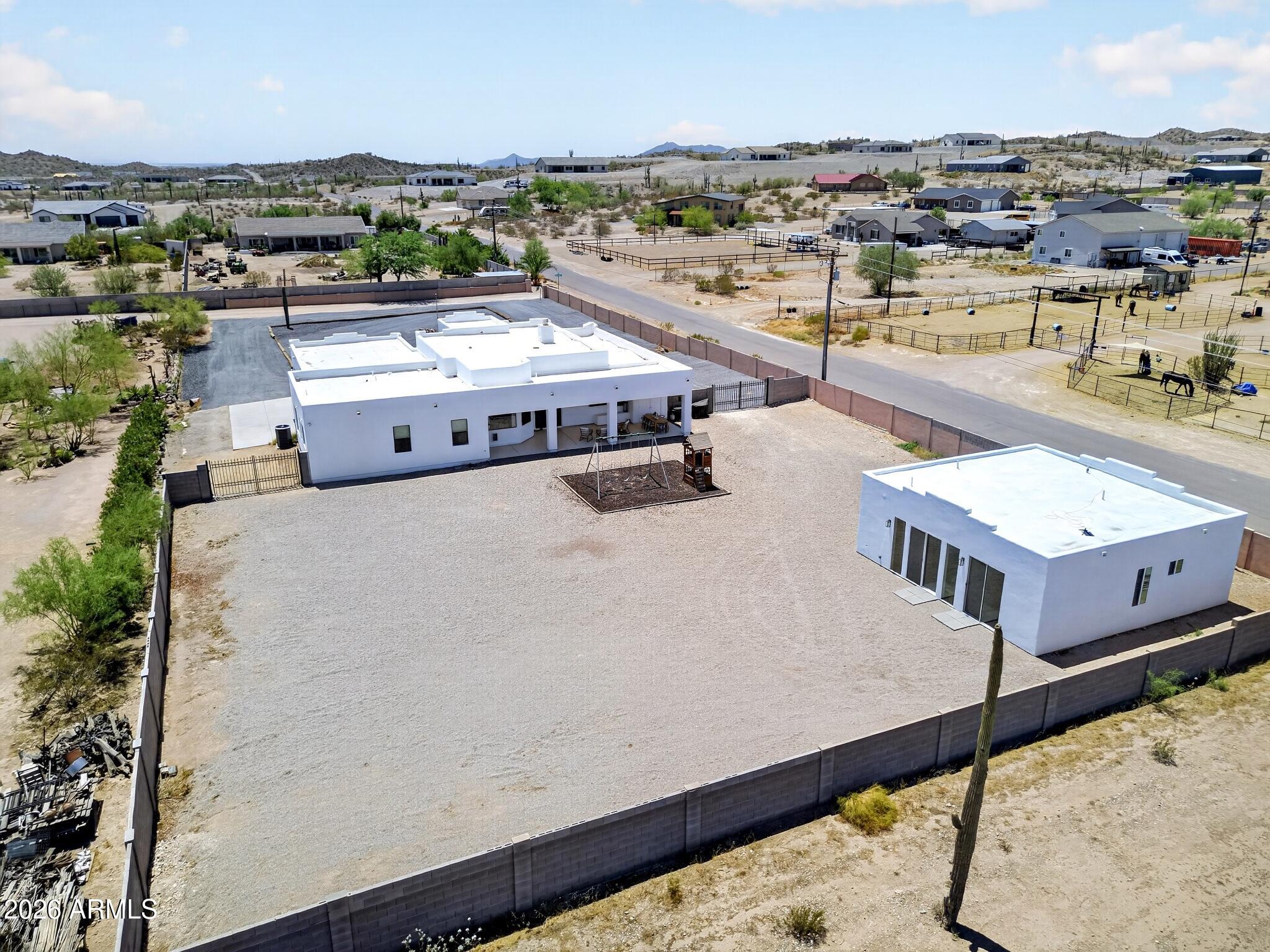 Aerial view of two white buildings in a walled desert property with a large gravel yard and playground.