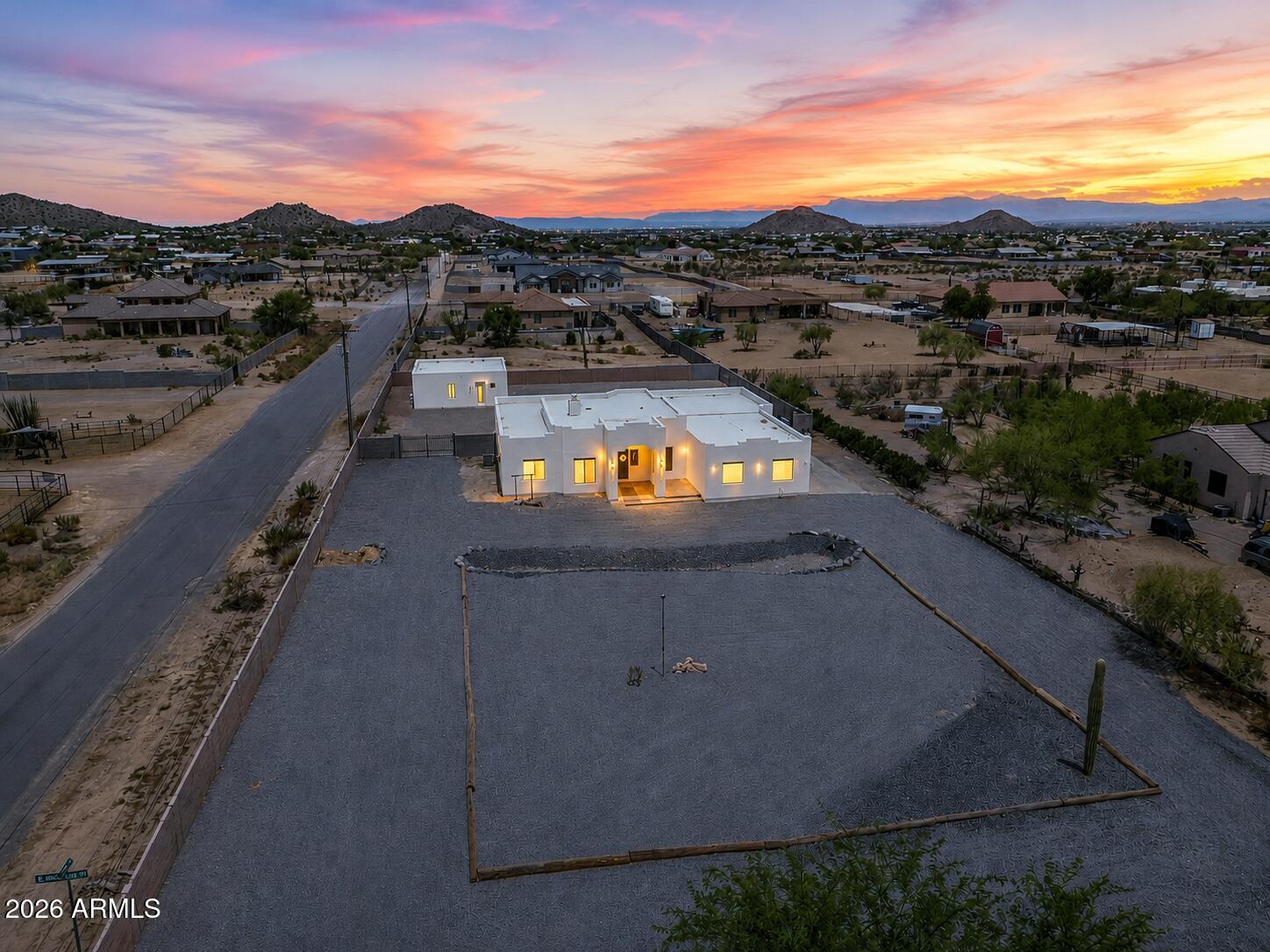 Modern white home on a broad gravel lot, with desert hills at sunset.