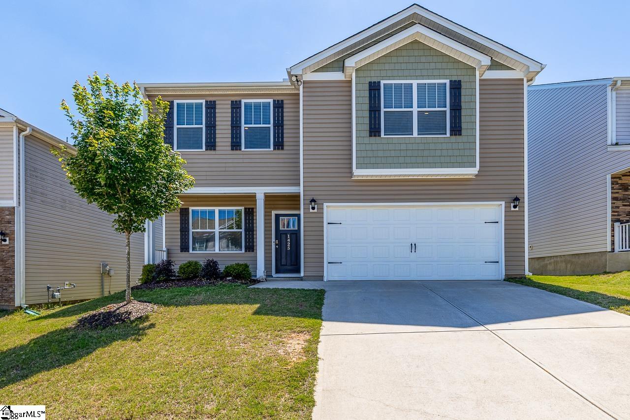 Two-story taupe house with a green upper-window accent, white double garage door, and front lawn.