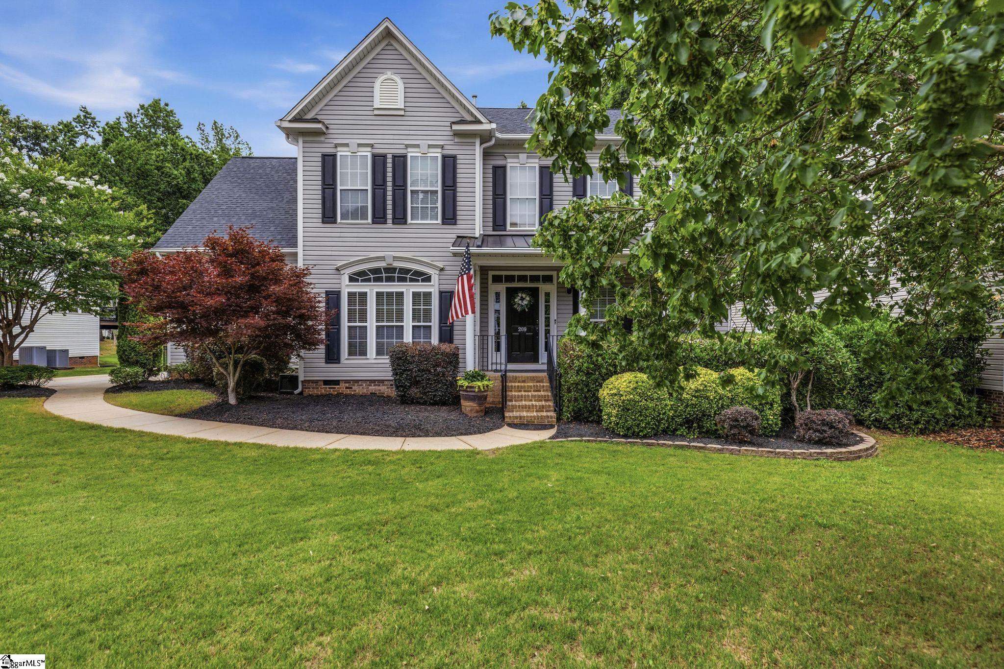 Two-story gray house with black shutters, brick entry steps, an American flag, and a curved front walkway.